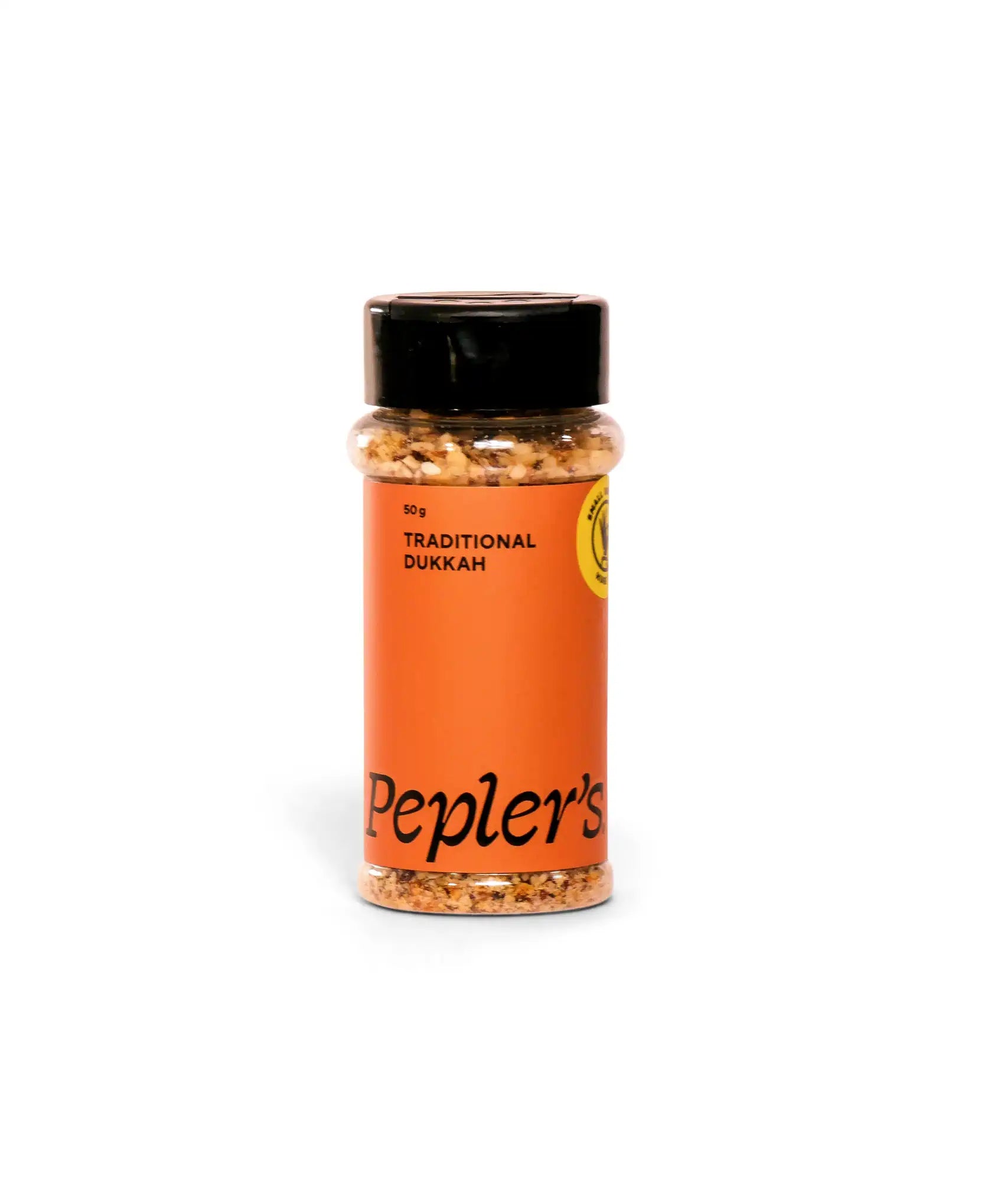 A clear plastic container of traditional dukkah spice mix with a black lid. The label features bold, black text on an orange background reading "Pepler's" and "Traditional Dukkah," along with a weight indication of 50 g. The spices inside are visibly a mix of crushed nuts and spices.