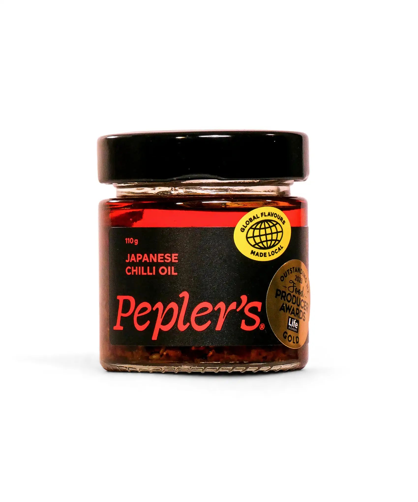 A close-up of a jar of Pepler's Japanese chilli oil, featuring a black lid and a vibrant red and black label. The label displays "110 g" and "JAPANESE CHILLI OIL" prominently, alongside a circular logo that reads "GLOBAL FLAVOURS MADE LOCAL" and another indicating "OUTSTANDING 2021 FOOD PRODUCERS AWARDS GOLD." The jar is set against a soft, neutral background.