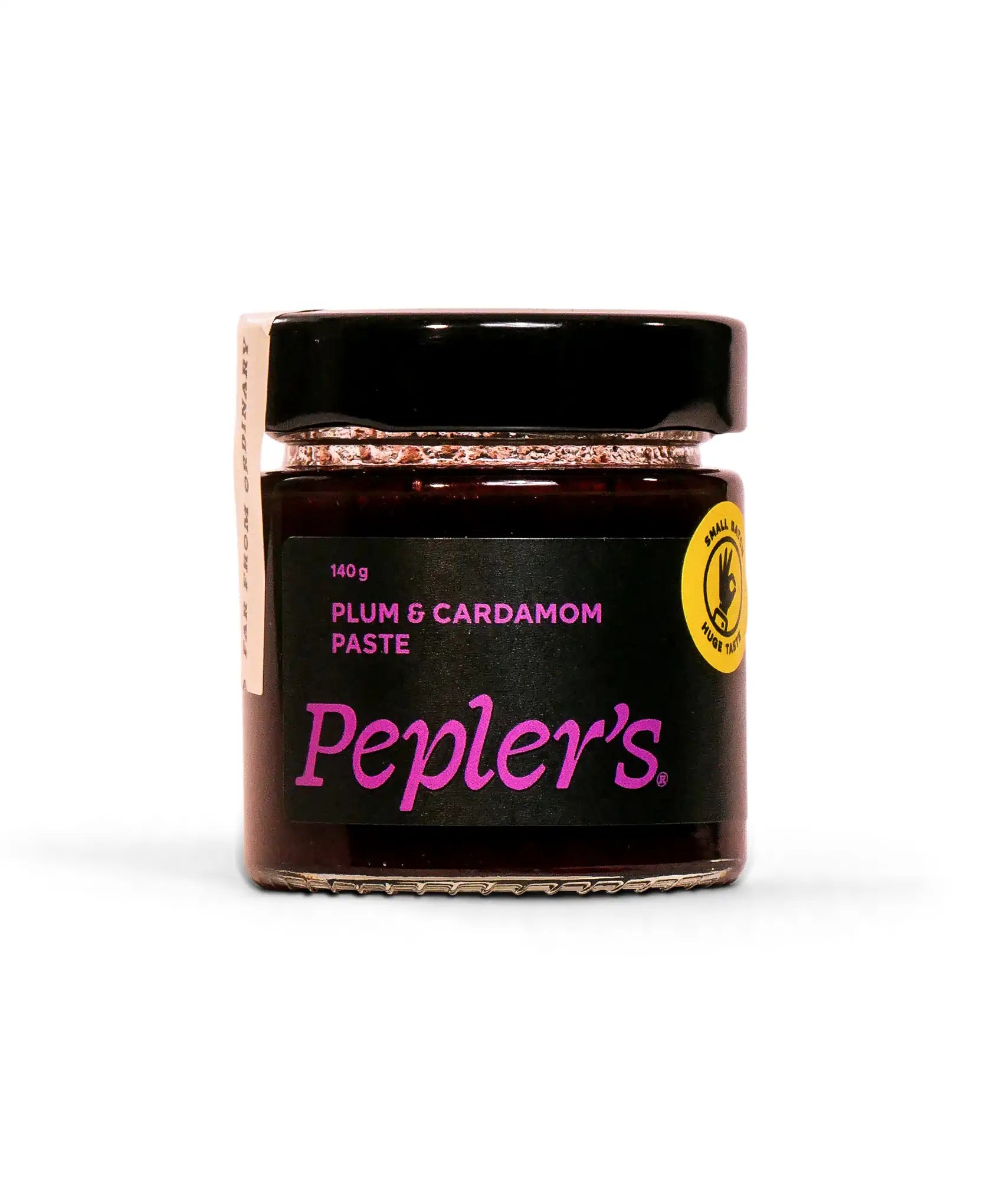 A clear glass jar containing plum and cardamom paste, featuring a black lid. The label is predominantly black with bright purple text stating "PLUM & CARDAMOM PASTE" and includes the brand name "Pepler's." The jar size is indicated as 140 grams, and a small circular logo in yellow suggests a focus on quality or natural ingredients. The background is plain and light-coloured, highlighting the jar.