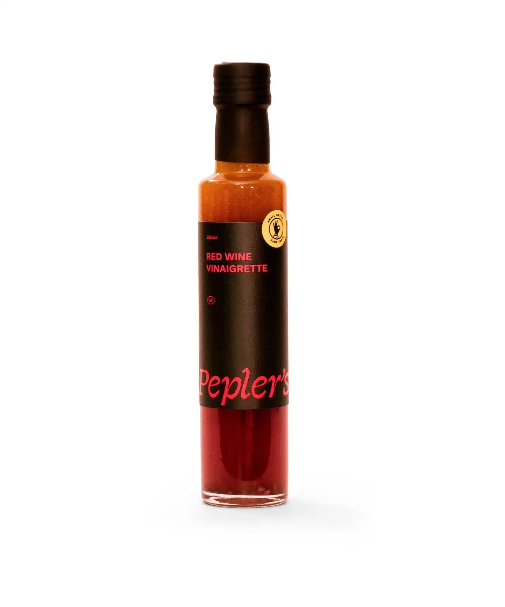 A bottle of Pepler's Red Wine Vinaigrette, 250ml, features a sleek design with a dark label. The label prominently displays the product name in pink text along with a gluten-free symbol and a small batch sticker. The vinaigrette inside the bottle has a rich red hue, suggesting a savoury dressing ideal for salads and marinades. The background is clean and white, highlighting the bottle's colours and branding.