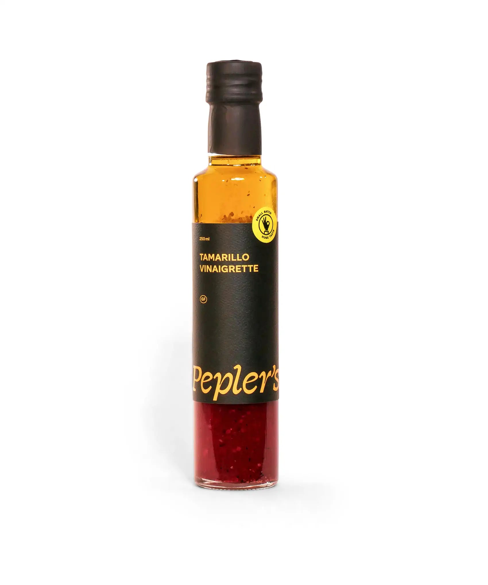 A clear glass bottle filled with tamarillo vinaigrette, labeled with a black and gold design. The bottle has a black cap and features the brand name "Pepler's" prominently, along with a yellow circular label indicating it is a small batch product. The vinaigrette has a vibrant reddish colour with visible flecks, suggesting rich ingredients. The total volume of the bottle is 250ml.